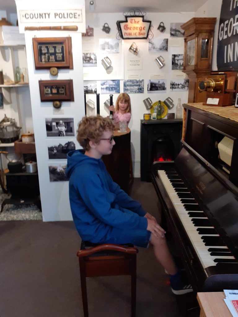 A boy sitting at the pianola with a girl behind.