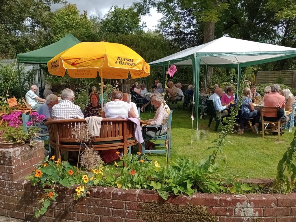 People sitting in a garden with chairs, tables and gazebos for a barbecue