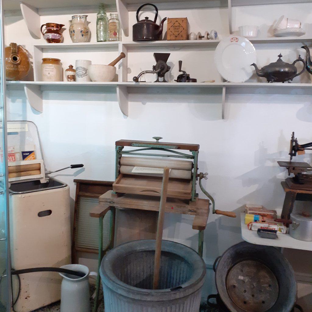 Old household equipment including a mangle, washing dolly and flagon.